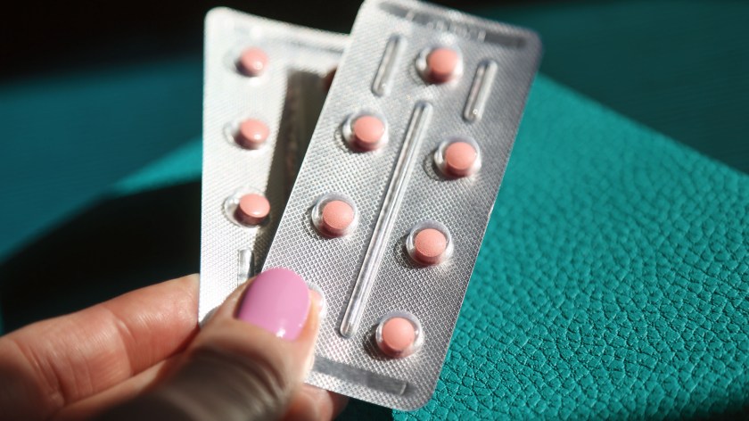 Woman's hand with pink nails holding two blister packs of HRT pills